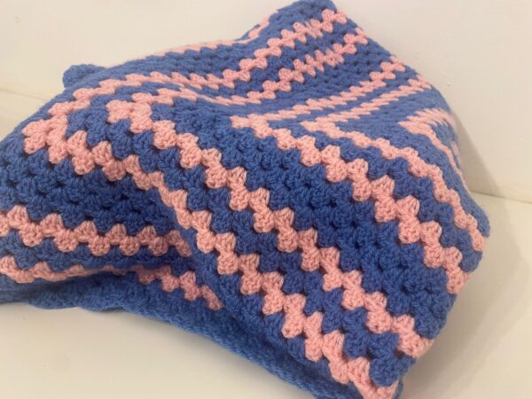 The Lorna Crochet Blanket, made with pink and blue wool, in a unique crochet design.