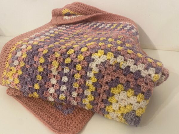 The Meabh, Large crochet blanket, made using a beautiful array of colours including pink, purple, yellow and white, in a unique design crochet pattern.